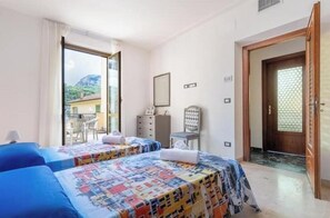 Une chambre avec deux lits, une chaise, une commode et une porte donnant sur un balcon.