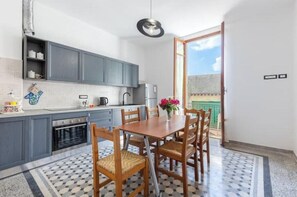 Une cuisine avec des meubles de couleur grise, une table à manger et des chaises, donnant sur un balcon.