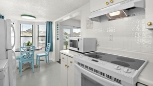 Una cucina compatta con mobili bianchi, un forno a microonde, un piano cottura e un'area pranzo con sedie blu.