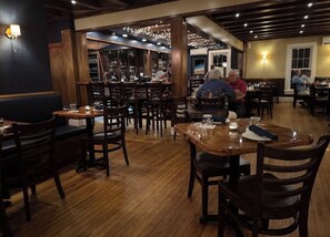 Ein Restaurant mit Holzböden, Tischen und Stühlen. Es gibt Barbereiche mit Regalen und Flaschen.