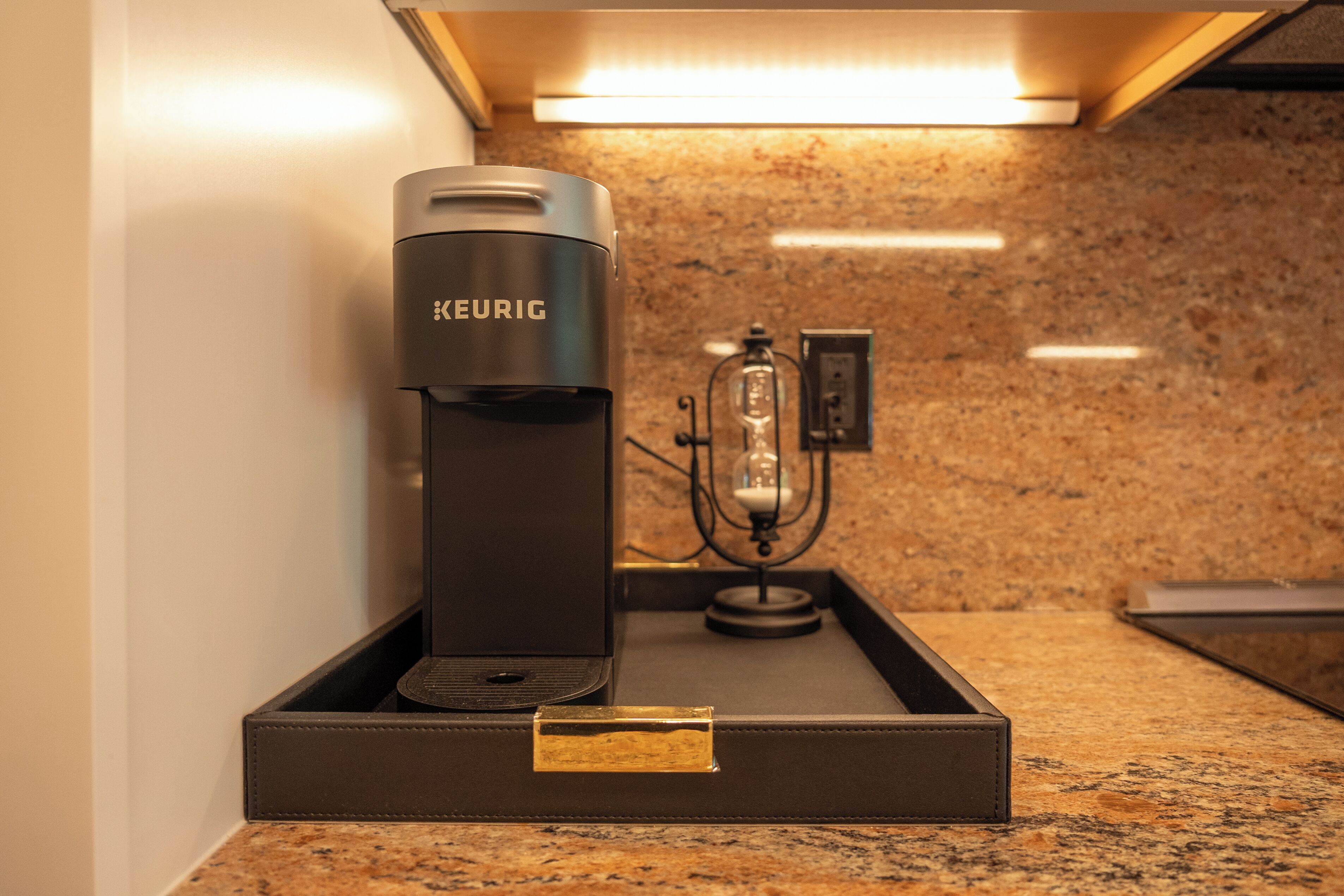 A KEURIG coffee machine in a black tray on a granite countertop.