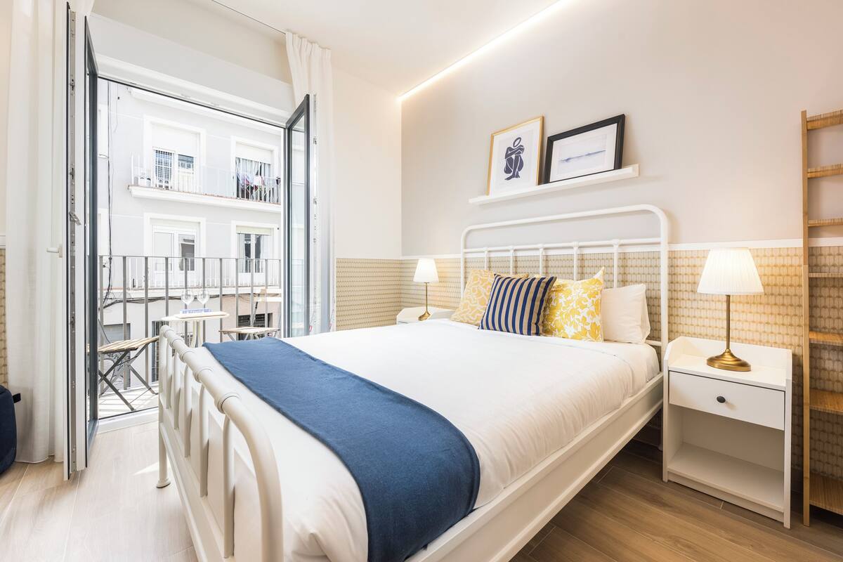 A bedroom with a bed, bedside tables, a lamp, a window, and a view of the outside.