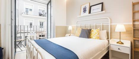 A bedroom with a bed, bedside tables, a lamp, a window, and a view of the outside.