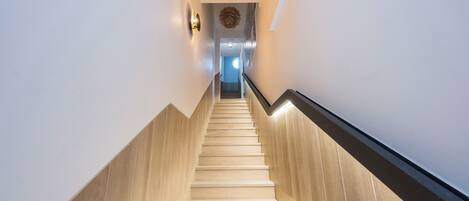 A modern staircase with wooden steps and a black handrail, leading to a room with a blue window and a circular light fixture.
