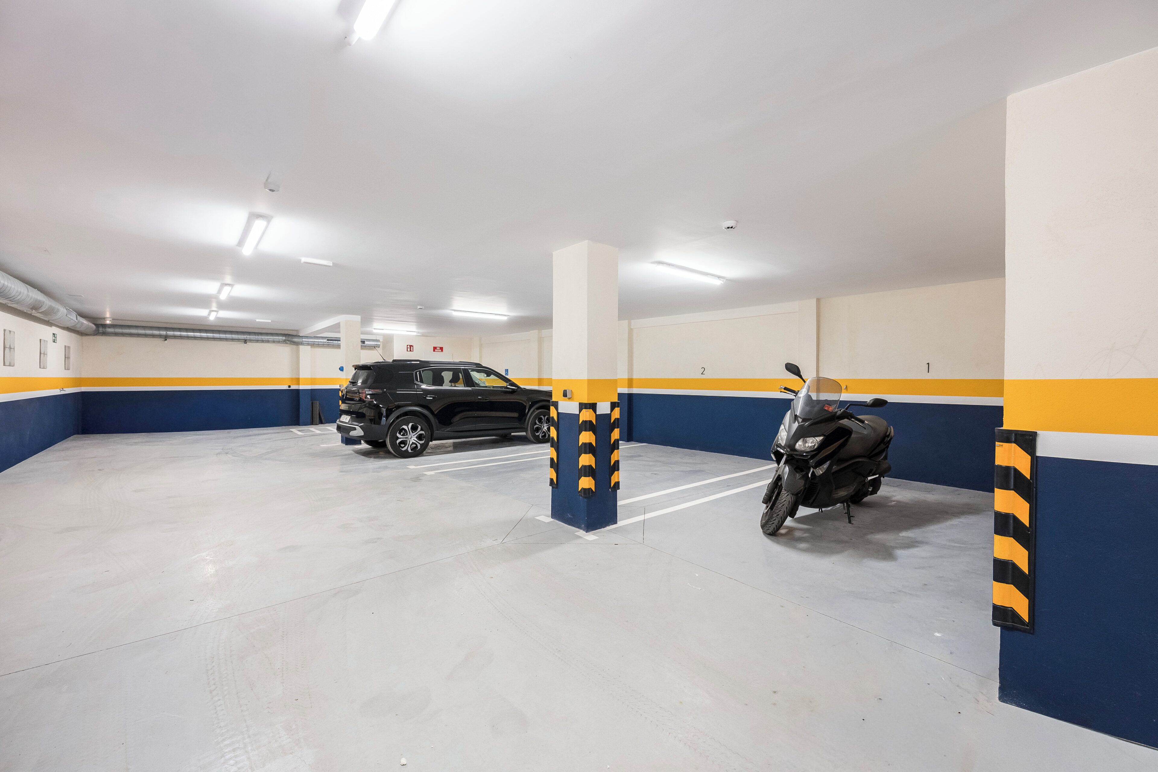 Un parking aux murs blancs et bleus, un SUV noir et une moto.
