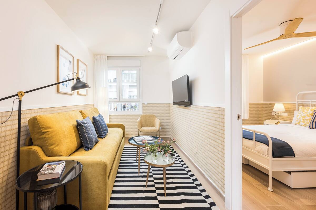 A compact living space with a sofa, a small coffee table, a bed, and a television.
