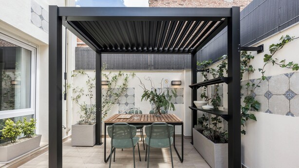 Un patio cubierto con una mesa y sillas, rodeado de plantas en macetas y una pared de azulejos.