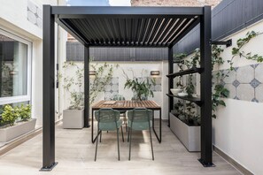 A covered patio with a table and chairs, surrounded by potted plants and a tiled wall. - Edmond Vibes Ventas (Madrid)
