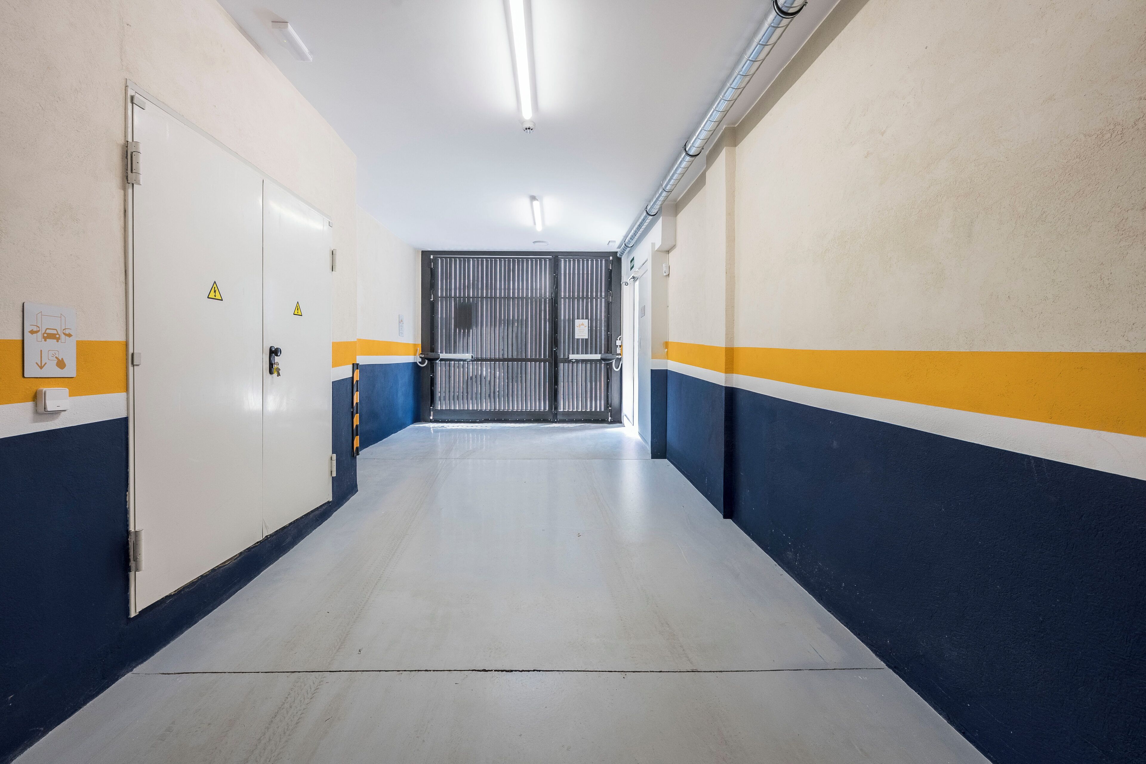 A corridor with a white door, a metal gate, and a yellow stripe on the wall.