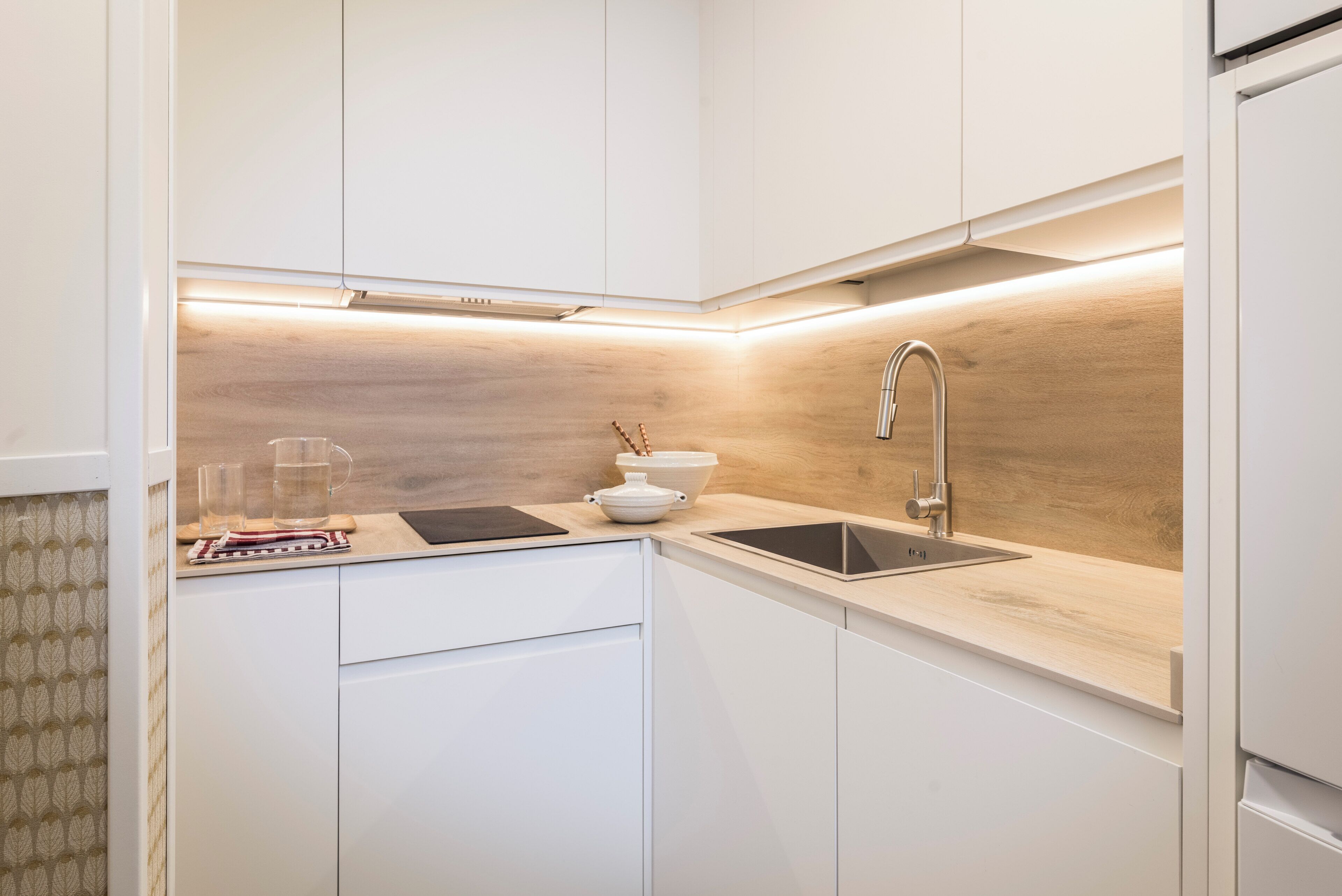 Una cocina moderna con armarios blancos, protector de salpicadero de madera, un lavamanos de acero inoxidable y un horno empotrado.