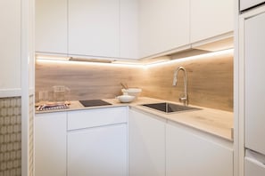 Una cocina moderna con armarios blancos, protector de salpicadero de madera, un lavamanos de acero inoxidable y un horno empotrado.