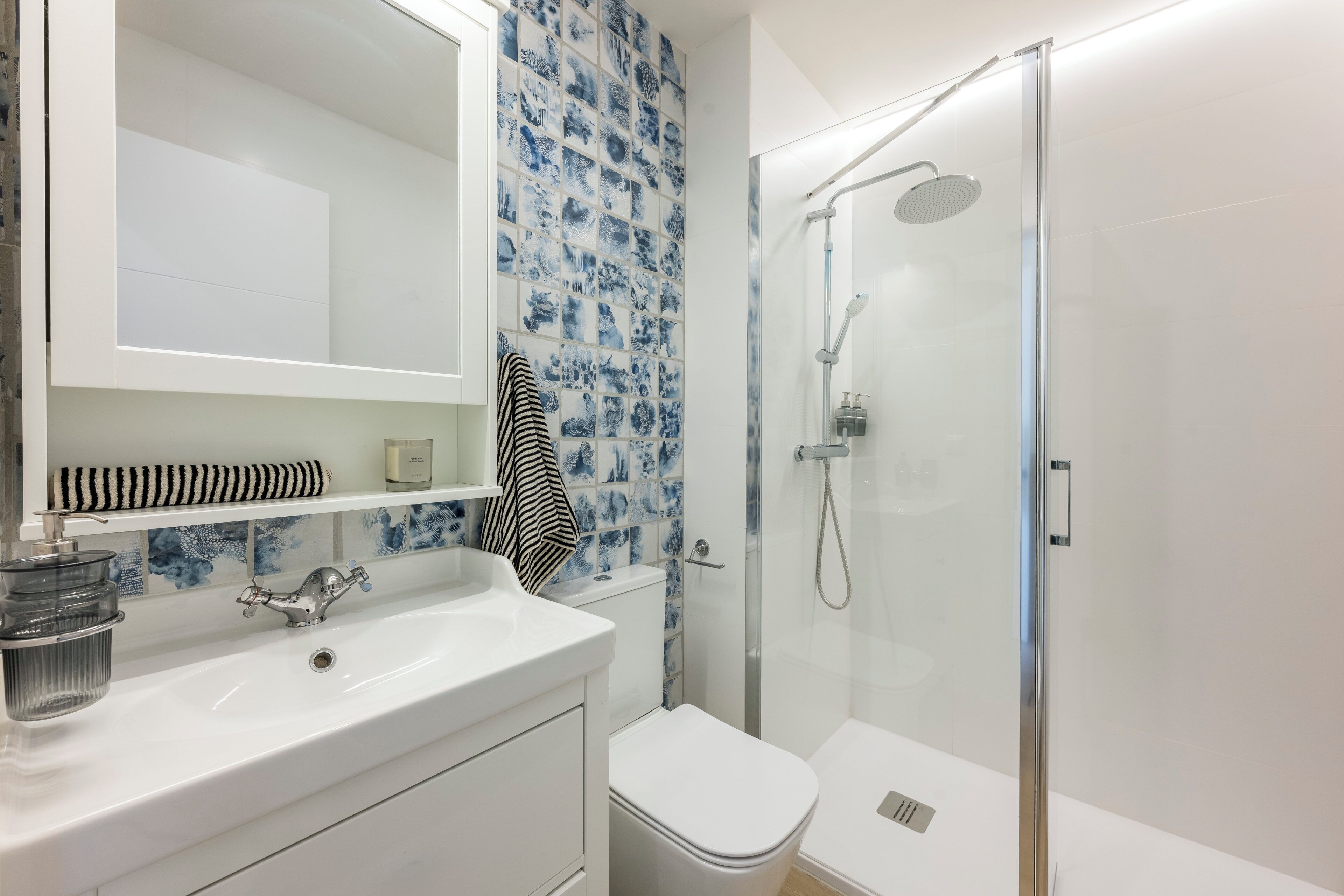 A modern bathroom with a white sink, a glass shower enclosure, and a blue-tiled wall.