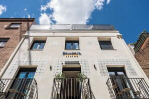 En byggnad med en skylt som visar texten ”Sambara Living”, balkonger med metallräcken och solpaneler på taket.
