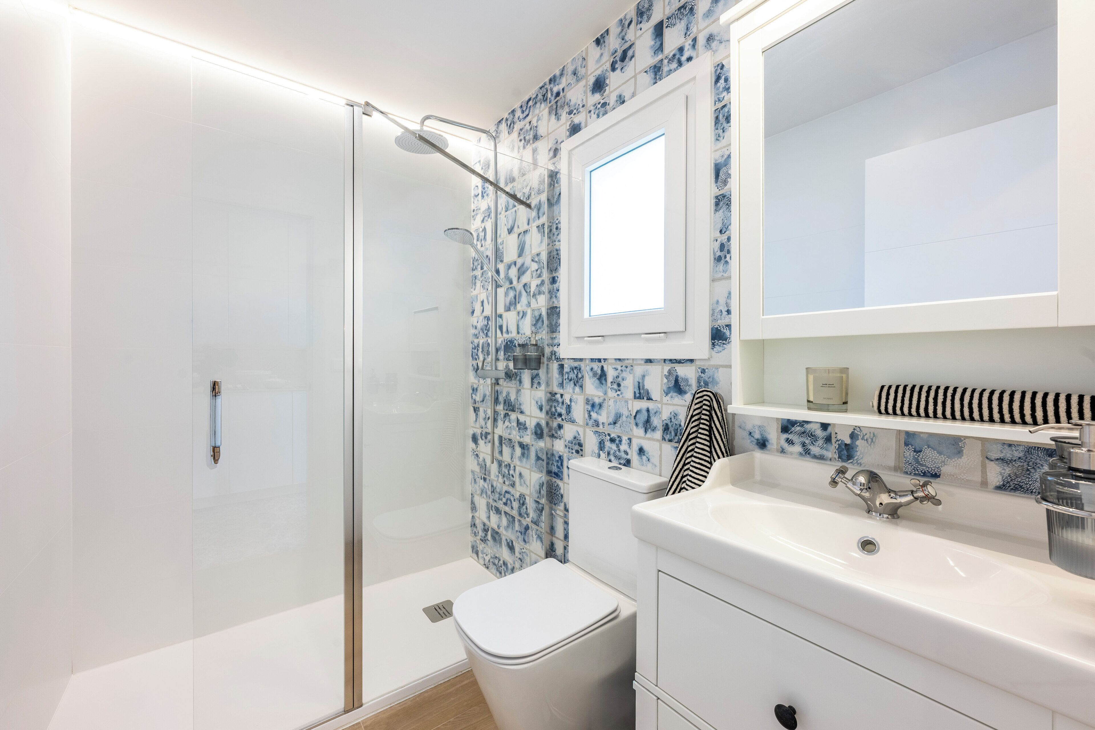 Een moderne badkamer met een douchecabine van glas, een toilet, een wastafel met spiegel en een betegelde spatwand.