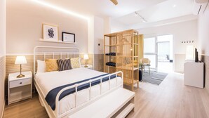 Habitación de hotel moderna con cama, mesitas de noche, ventilador de techo, armario y escritorio.
