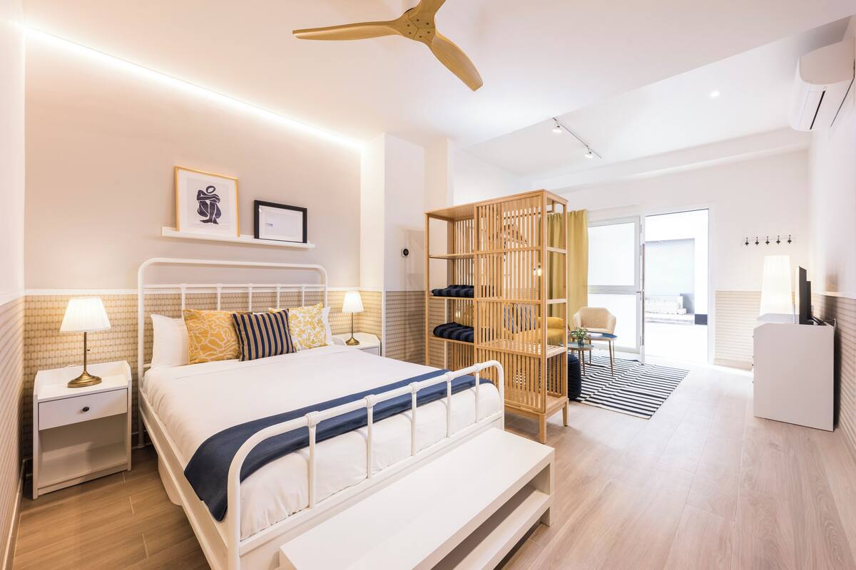 A modern hotel room with a bed, bedside tables, a ceiling fan, a wardrobe, and a desk.
