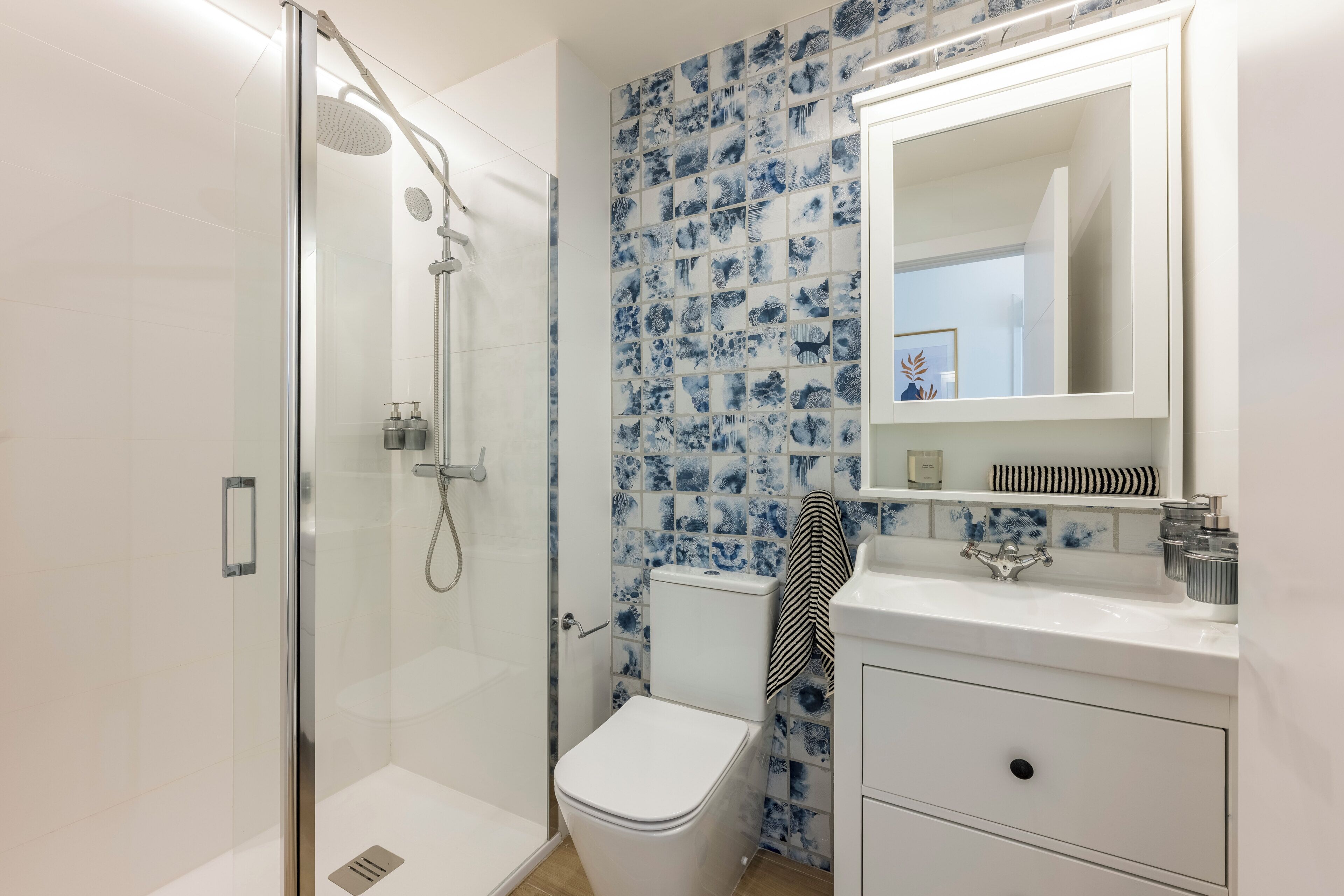 Un baño moderno con ducha envuelta en vidrio, inodoro y lavamanos con espejo.
