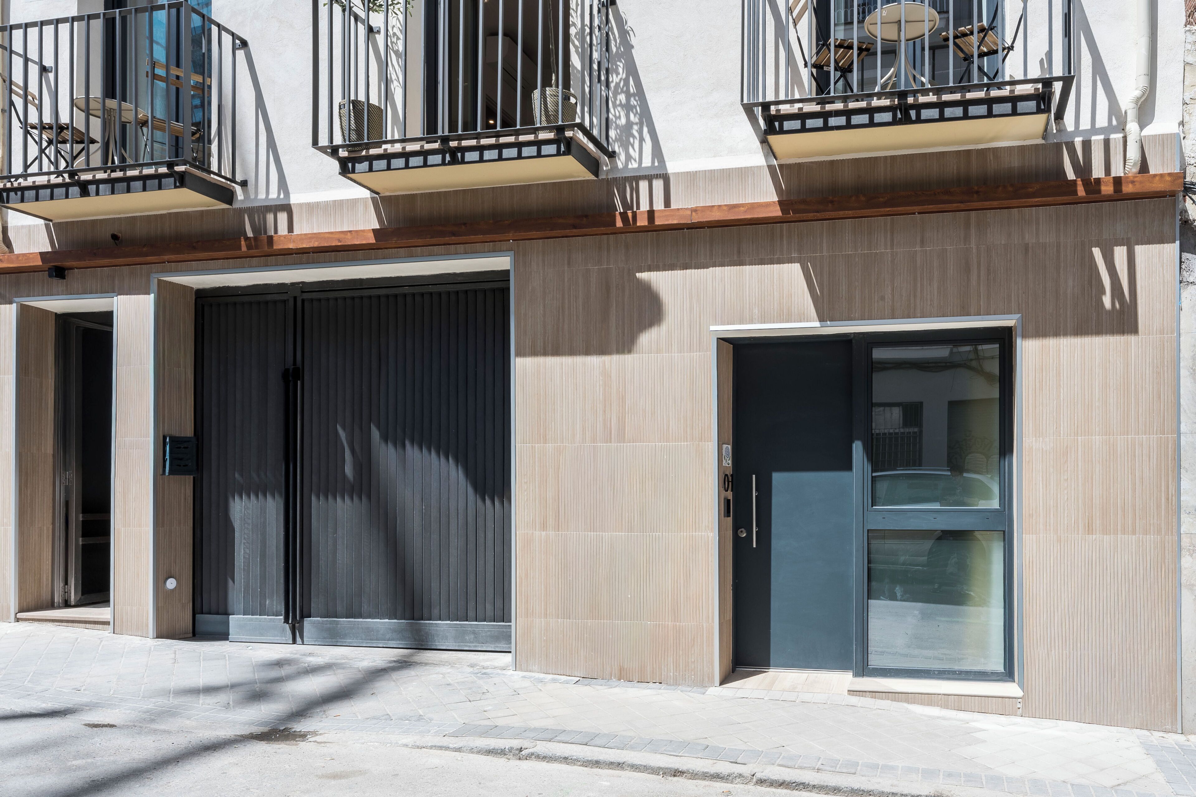 Un bâtiment moderne doté d’un grand portail de garage, d’un balcon avec une table et des chaises, et d’une porte avec une fenêtre.