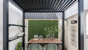 Un espacio exterior moderno para comer con una mesa de madera, dos sillas, una planta en maceta y una pared verde.