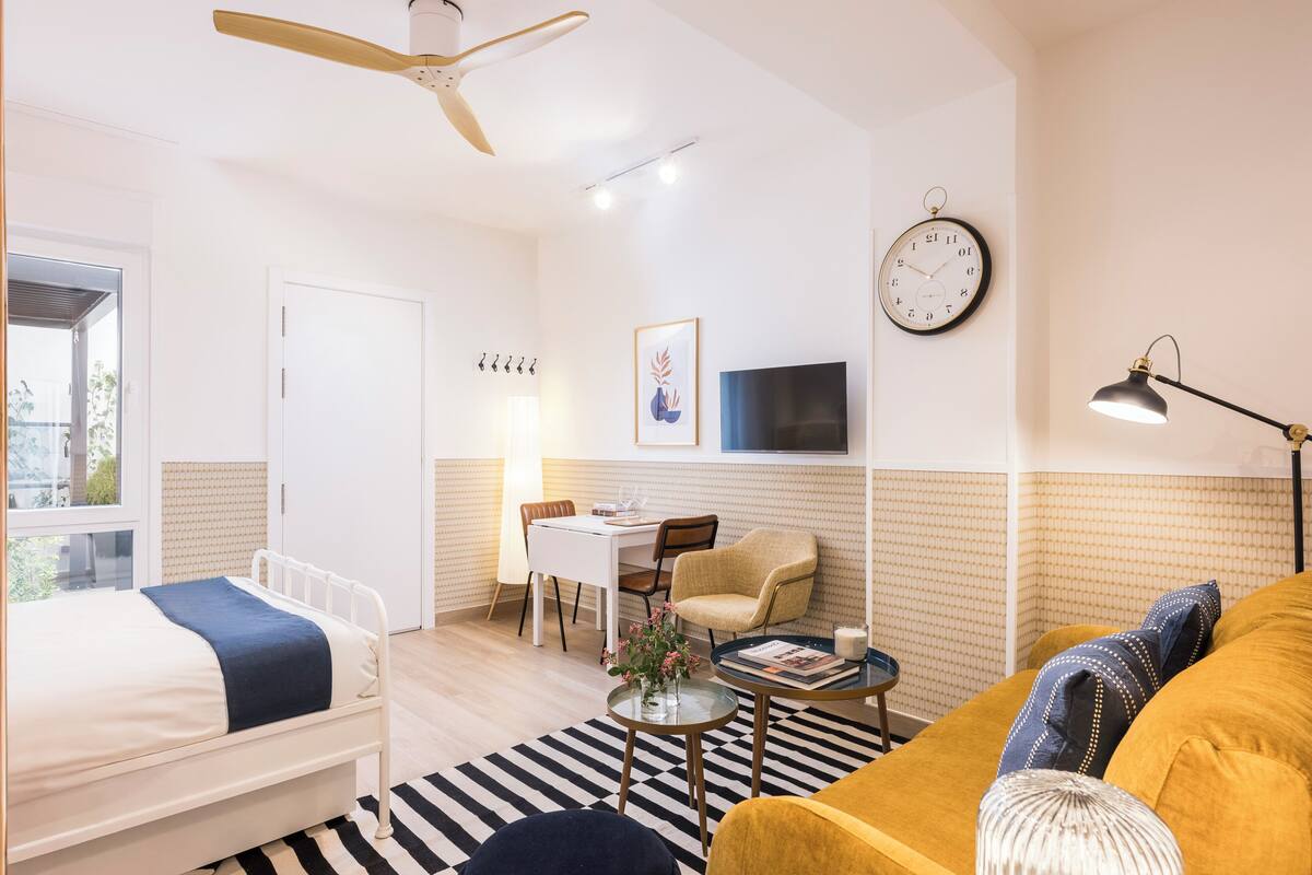 A modern room with a bed, a sofa, a dining area, a TV, and a ceiling fan.