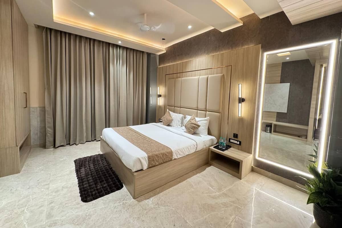 A modern hotel room with a large bed, a bedside table, a mirror, and a potted plant.