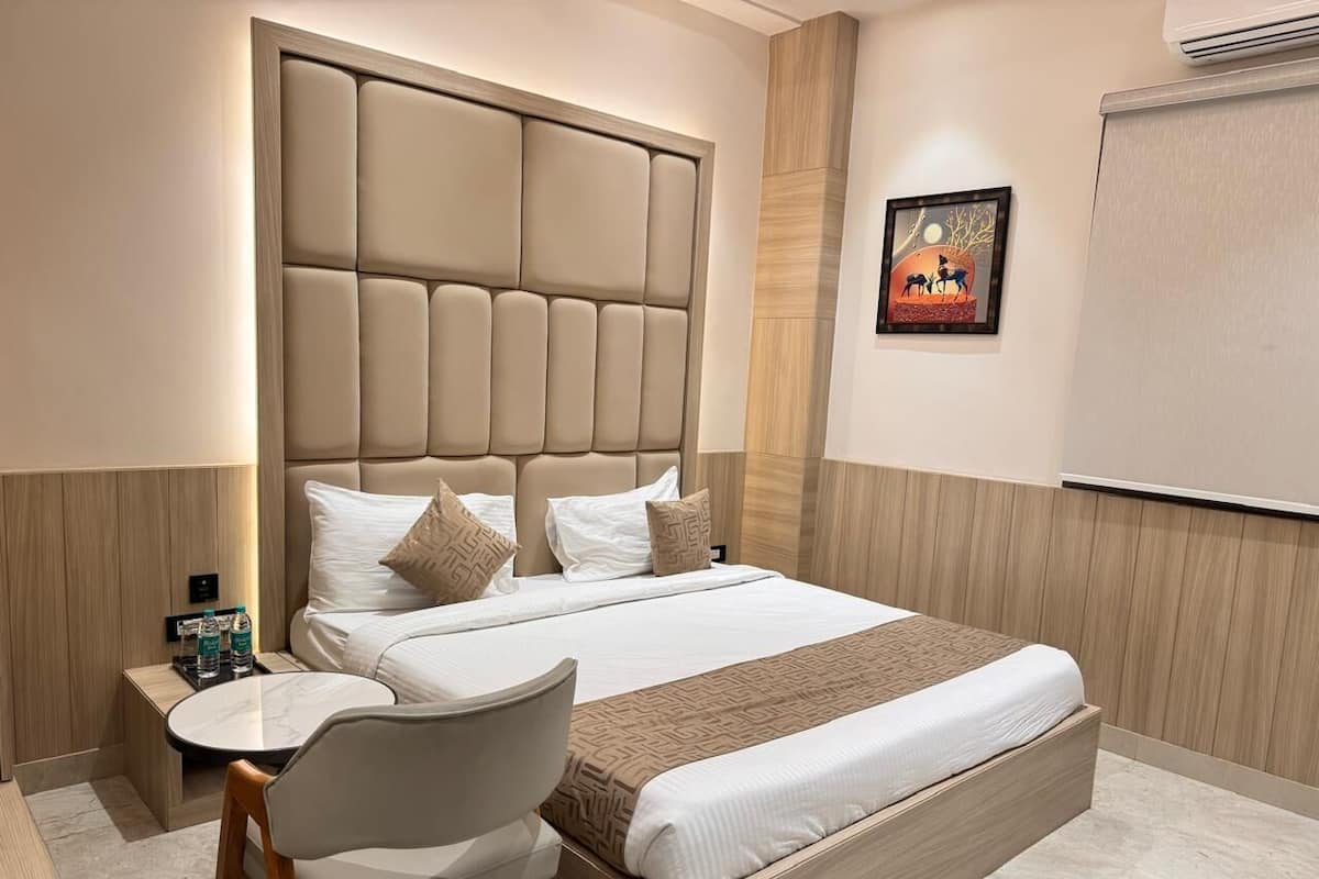 A hotel room with a large bed, a bedside table with a lamp, a chair, and a small table with water bottles.