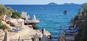 Une zone côtière avec une jetée en pierre, des chaises longues bleues et des parasols.