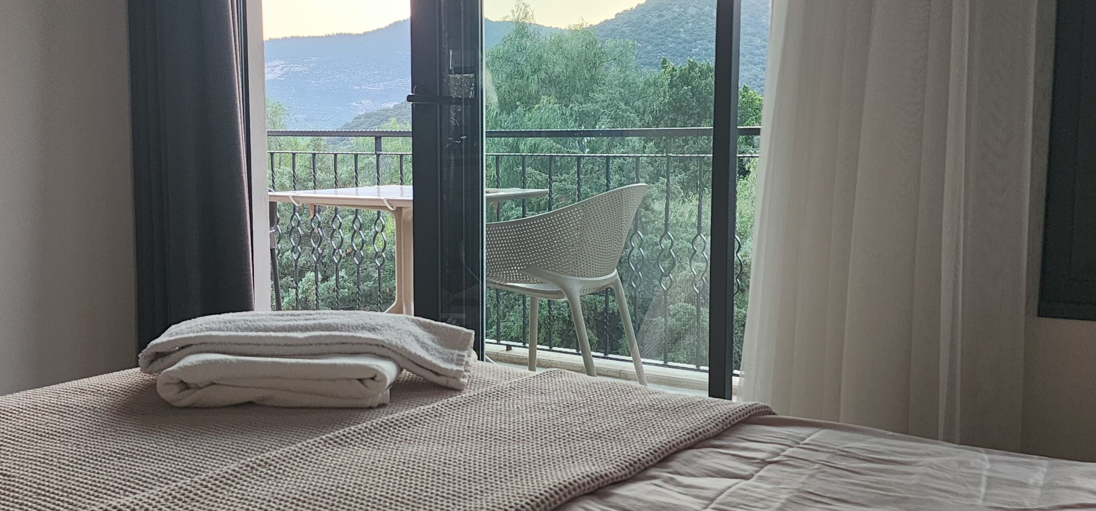 A room with a bed, a window with a view of a balcony and mountains.