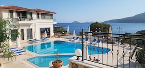 Un espace piscine offrant une vue dégagée sur la mer, un bâtiment doté d’un balcon et de chaises longues.