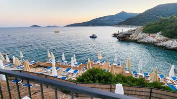 A coastal view with a wooden deck, lounge chairs, and umbrellas overlooking the sea.