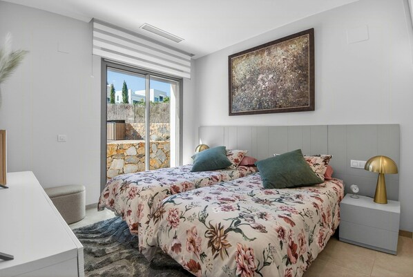 A bedroom with a bed, a nightstand, a lamp, a painting, and a view of the outside. - Luxury villa in Las Colinas Golf, Orihuela (Orihuela)