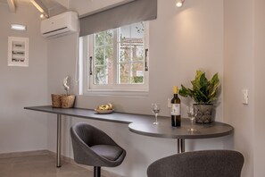Eine moderne Küche mit Fenster, einem Esstisch, zwei Stühlen, einer Topfpflanze, einer Weinflasche und einer Obstschale.