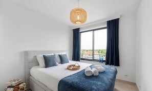 Ein Hotelzimmer mit Bett, einem großen Fenster mit Vorhängen, einer Hängelampe und Blick auf Gebäude.