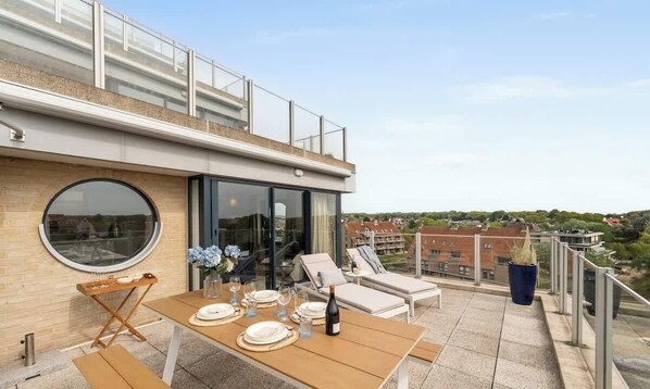 Una terraza en la azotea con una mesa de comedor para dos, sillas de lounge y vistas del entorno.