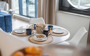 Ein runder Esstisch mit Platzsets, einer Kaffeekanne, Tassen und einer Schüssel mit Müsli.