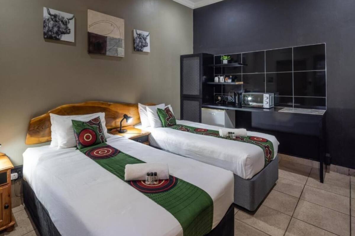 A hotel room with two beds, a desk, a microwave, and a shelf with items.