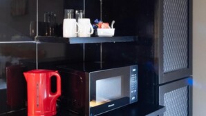 Una cocina con microondas, una tetera roja y estantes con utensilios de cocina.
