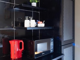 Una cocina con microondas, una tetera roja y estantes con utensilios de cocina.