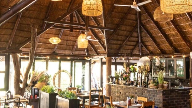 Un restaurante interior con mesas y sillas de madera, y un techo de paja.