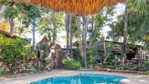 Una piscina en un entorno natural, con árboles y una estructura de techo de paja.