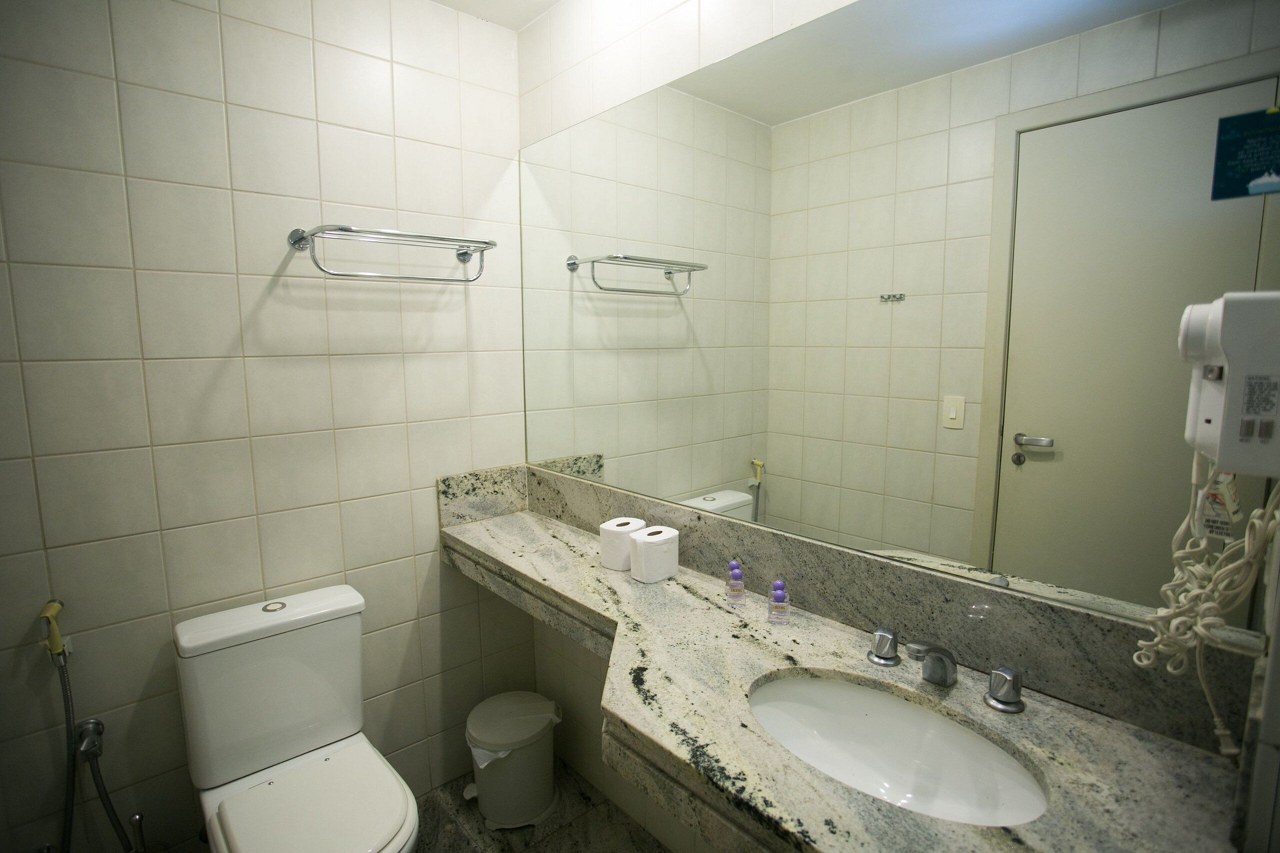 A bathroom with a toilet, sink, mirror, and towel rack.