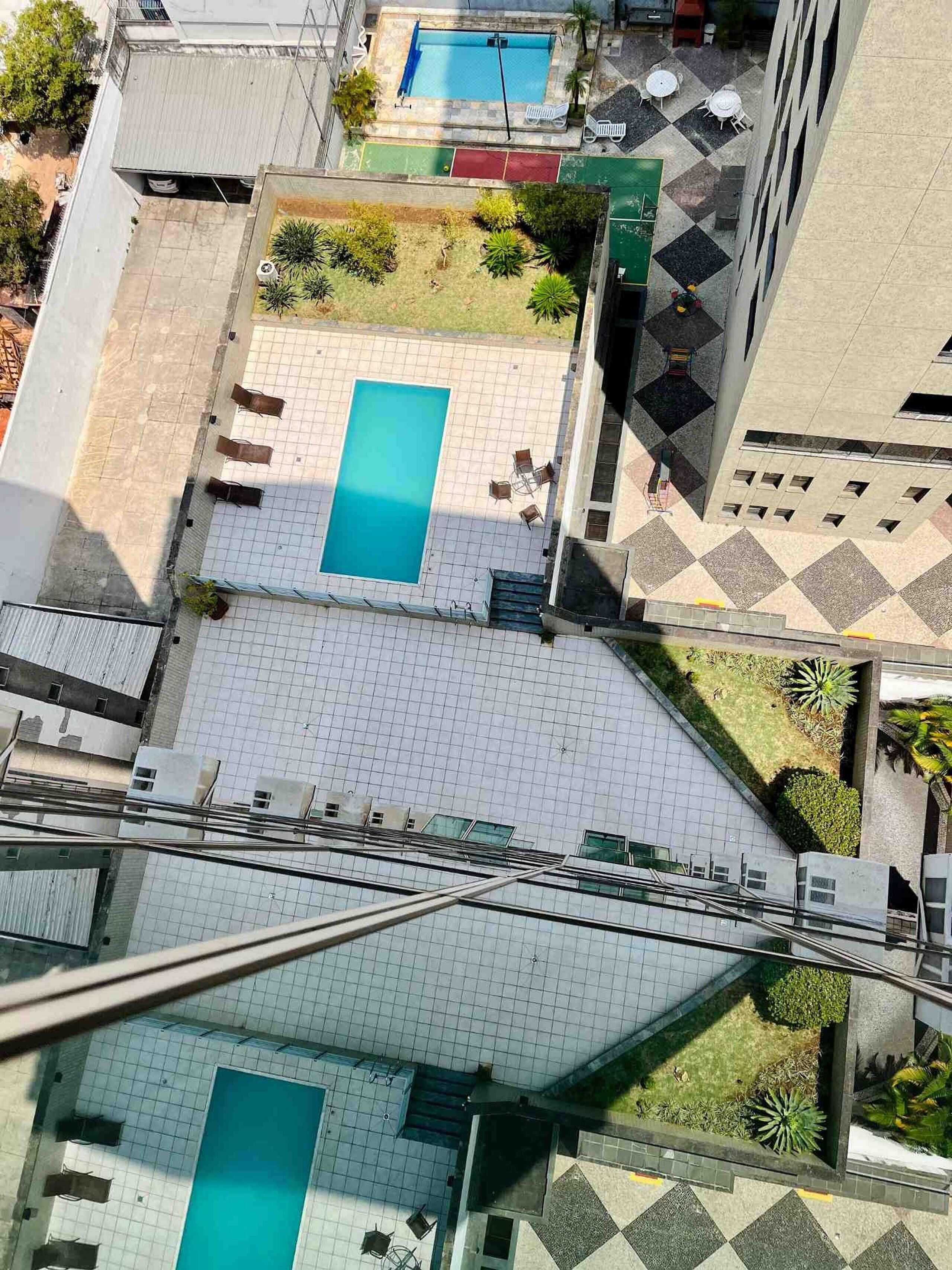 Vista aérea de um edifício com duas piscinas, áreas de estar ao ar livre e um pátio ladrilhado.