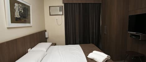 A hotel room with a bed, a TV, a painting on the wall, and a telephone.