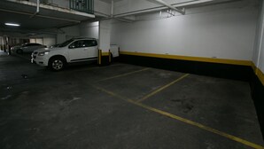 Un estacionamiento subterráneo con pisos de concreto, espacios delimitados y un automóvil blanco estacionado en uno de ellos.