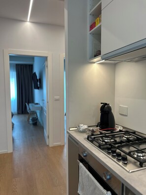 A modern kitchen with a gas stove, a kettle, and a microwave. There is a dining area visible in the background. - 4BNB - Stiv's Apartment (Rome)