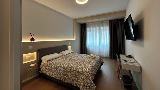 Ein Hotelzimmer mit Bett, Nachttisch, Fernseher und einem Fenster mit Vorhängen.