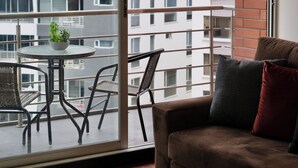 A balcony with a table and chairs, a brown sofa, and a view of a modern building. - Livorno Suites (Quito)