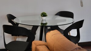 A modern dining area with a round glass table, black chairs, a single hanging light fixture, and a small plant on the table. - Livorno Suites (Quito)