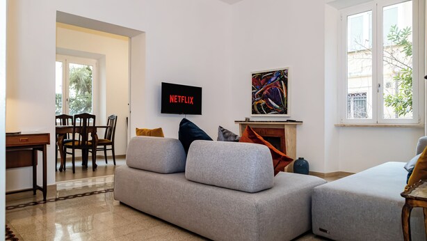 A living room with a grey sofa, a TV mounted on the wall, and a fireplace.