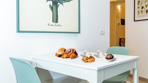 A dining area with a white table, teal chairs, and a framed botanical illustration on the wall.